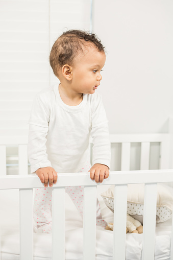 Cute baby standing in the crib in bedroom