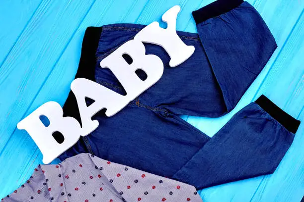 Baby-boy jeans and shirt on sale. Kids attire for casual wear, blue wooden background. Shop infant boy brand apparel.