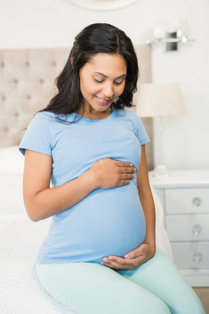 istock Smiling pregnant brunette sitting on bed 845772782