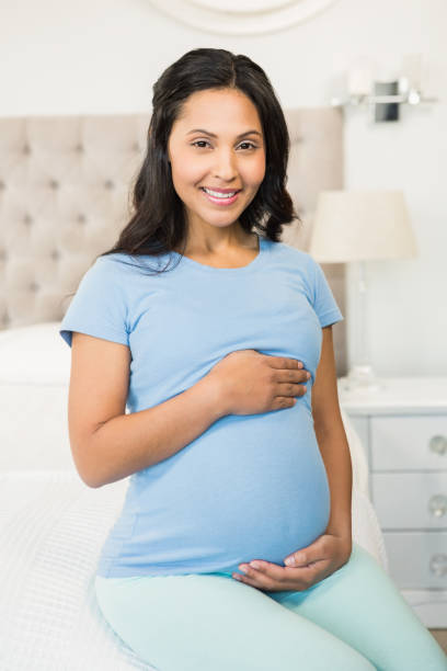 istock Smiling pregnant brunette sitting on bed 845772794