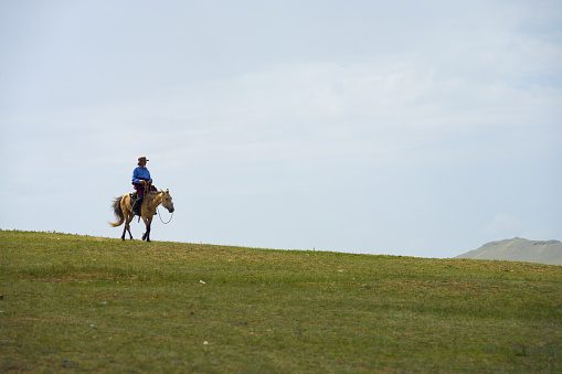 Mongolian man on horseback against a cloudy sky riding horse down a hill on the steppe in the countryside