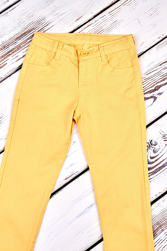 Young woman middle waist trousers. Yellow cotton pants for girls on old wooden background. Female summer outfit.