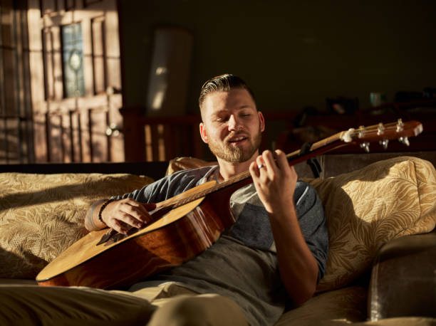 man playing guitar on sofa at home - plucking an instrument imagens e fotografias de stock