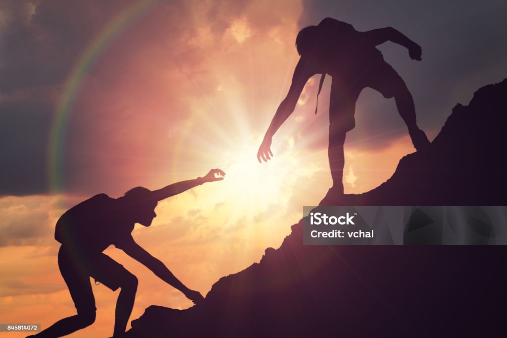 Mann ist eine helfende Hand geben. Silhouetten von Menschen klettern am Berg bei Sonnenuntergang. - Lizenzfrei Eine helfende Hand Stock-Foto