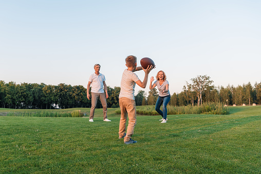 little boy going to throw rugby ball while playing american football with grandparents on green lawn