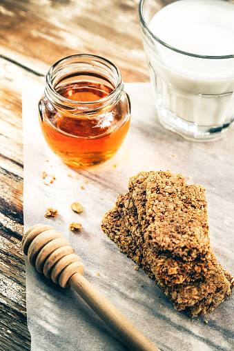 Stack of granola bars,glass of milk and jar of honey on rustick wooden table.