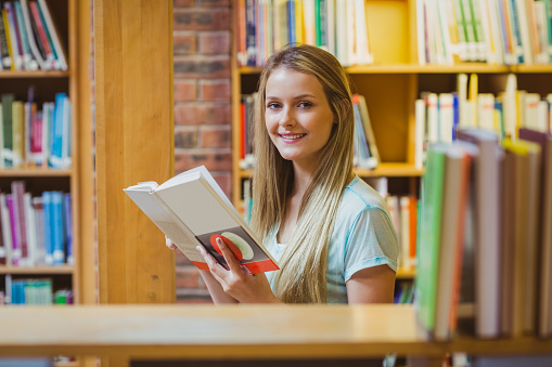 Pretty young blonde reading book in library