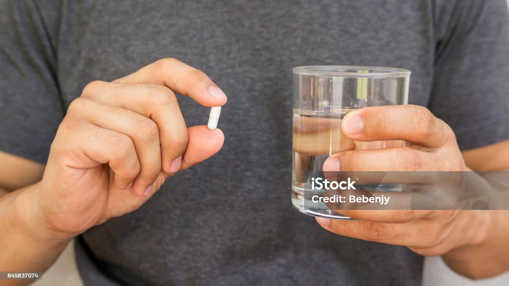 Man holding a pill and a glass of water. Men Stock Photo