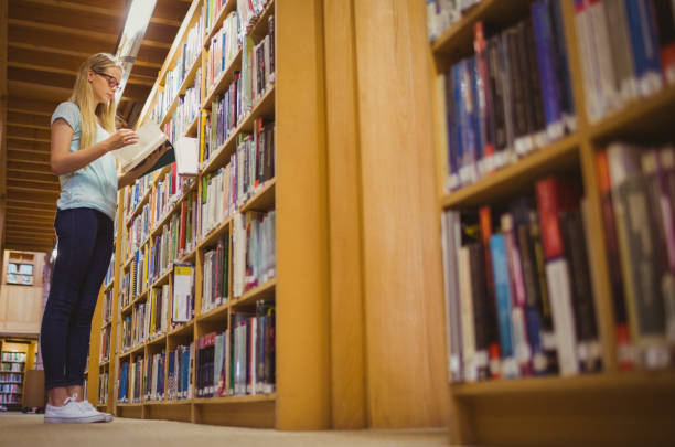 istock Blonde student reading book next to bookshelf 845839420