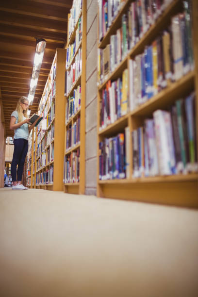 istock Blonde student reading book next to bookshelf 845839438