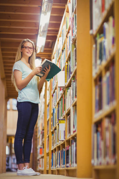 istock Blonde student reading book next to bookshelf 845839490