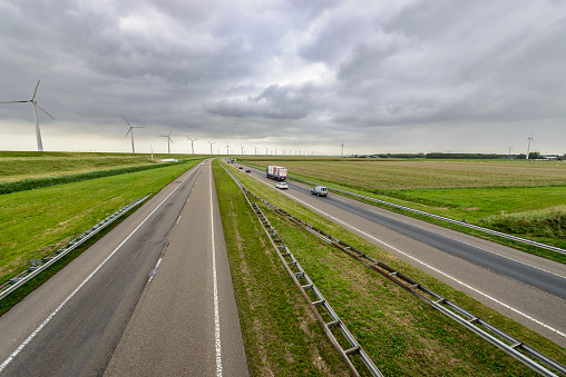 Traffic on a highway in an open rural landscape with windturbines. Cars are driving on the road in two directions.