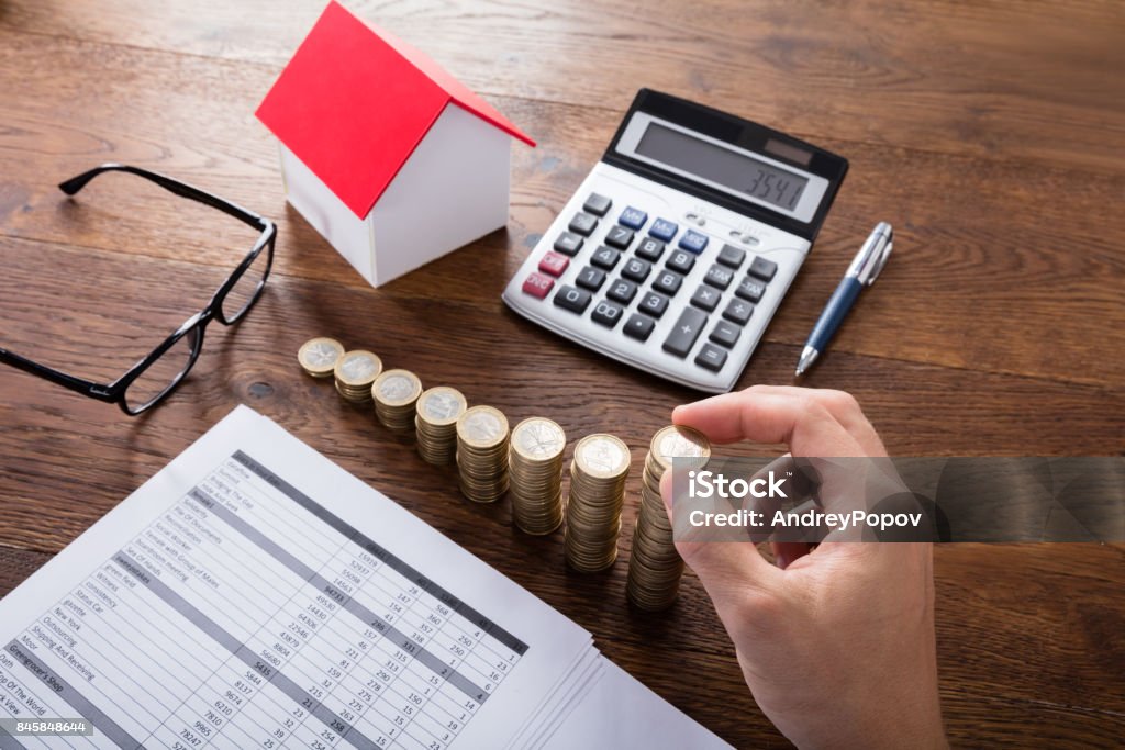 Person Stacking Coins On Wooden Desk High Angle View Of A Person Stacking Coins Near House On Wooden Desk. Property Tax Concept Adult Stock Photo