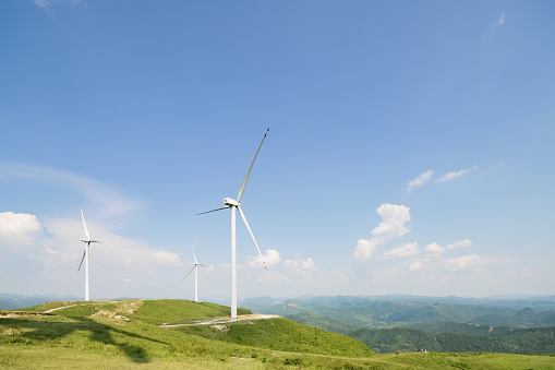 Wind turbine power generator standing on hill against beautiful blue sky. Sustainable resources background
