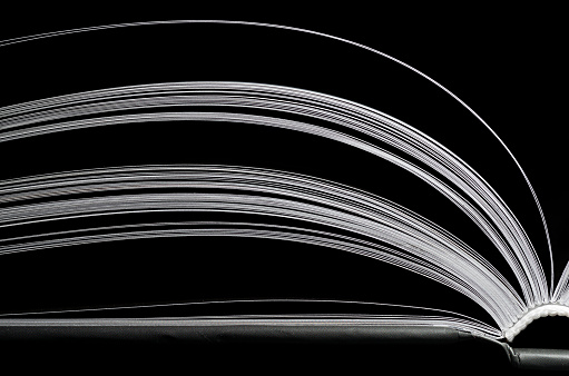 A black and white image of open book. Close-up image of pages on black background. Concept of gaining knowledge, education, learning, typography, passion for reading