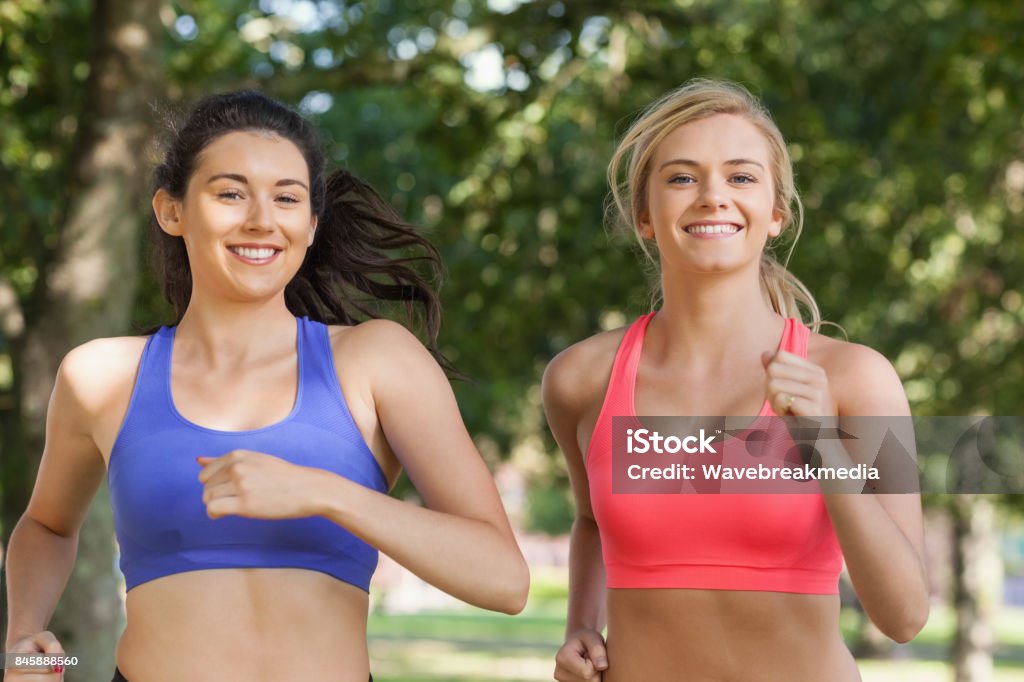 Two beautiful sporty women jogging in a park Two beautiful sporty women jogging in a park smiling at camera Friendship Stock Photo