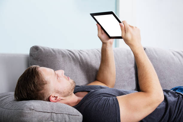 istock Man Lying On The Couch Looking At Digital Tablet 845895934