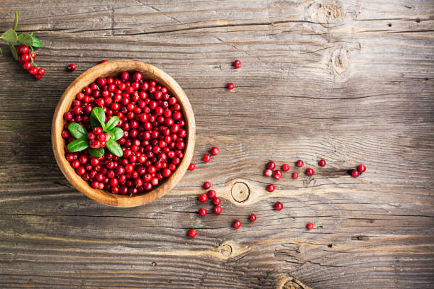 istock Red lingonberry in wooden bowl on rustic surface, top view 845896538