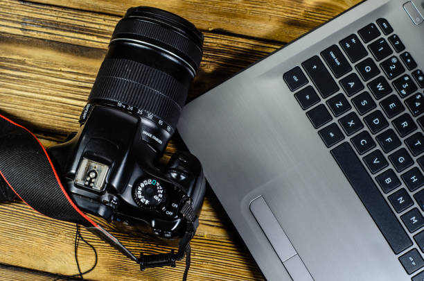 istock Modern DSLR camera and laptop on wooden table. Top view 845909568