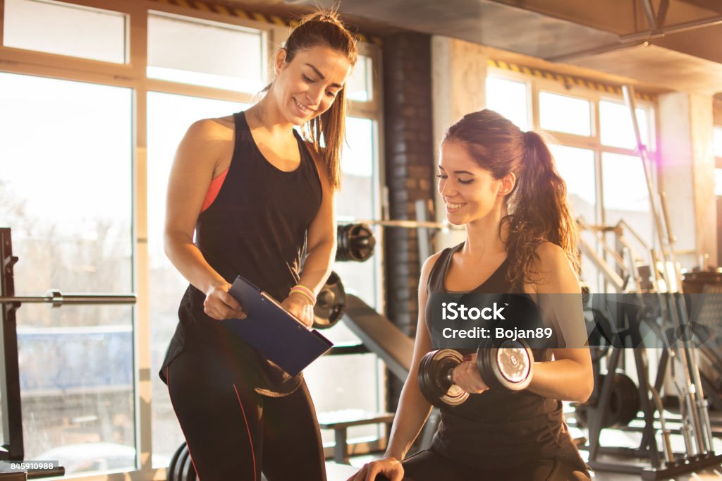 Femme fitness formateur montrant exercice progrès sur presse-papiers à jeune femme sportive au gymnase. - Photo de Instructeur de fitness libre de droits