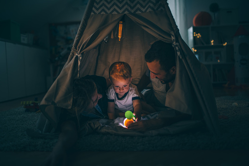 Photo of a young family with one child, reading bedtime stories in their boy's wigwam