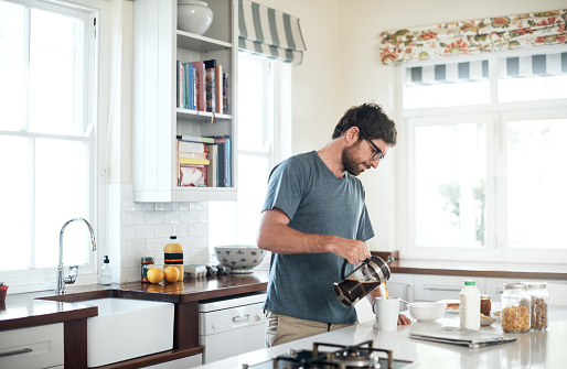 Shot of a young man making his morning coffee in the kitchen at home