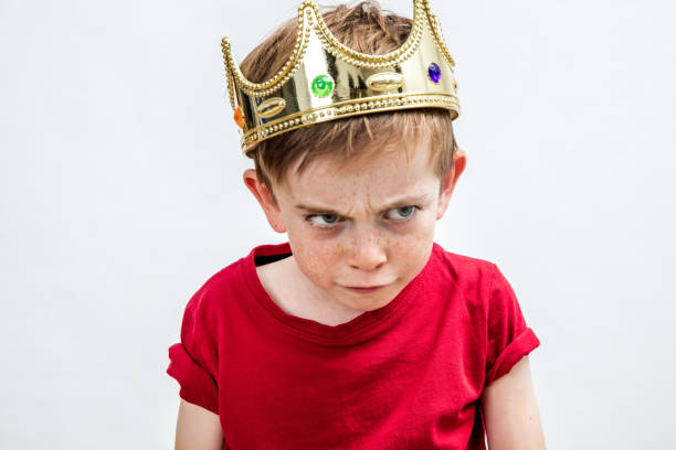 angry beautiful spoiled kid with frowning freckles wearing a king crown for mad attitude facing unhappy parenthood and education, white background, copy space