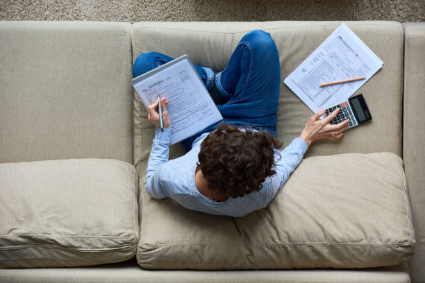 Tax-preparation at home Directly above view of concentrated accountant using calculator while preparing tax forms sitting on sofa filing paperwork stock pictures, royalty-free photos & images