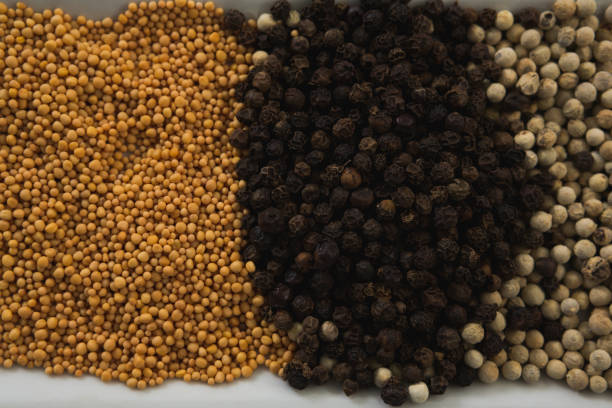 A pile of yellow mustard seeds scattered on a clean white background. The tiny, round seeds create an interesting texture and visual pattern, often associated with spice, flavor, and natural ingredients. Ideal for culinary and food-themed concepts.