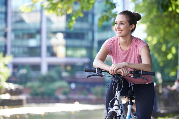 Young Woman Cycling Next To River In Urban Setting stock photo