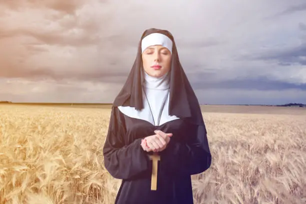 Young serious nun with cross on wheat field background