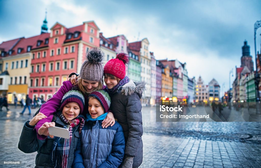 Family sightseeing city of Wroclaw in autumn Mother with three kids taking selfie in Wroclaw main square. Family is sightseeing the city on cold autumn day evening. Sightseeing is fun even in the bad weather! Family Stock Photo