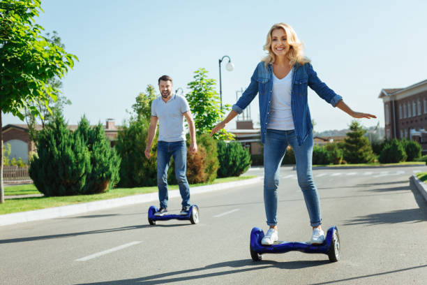 Happy husband and wife riding self-balancing scooters Satisfied with purchase. Joyful young husband and wife riding hoverboards and smiling happily, being pleased with their new purchase hoverboard stock pictures, royalty-free photos & images