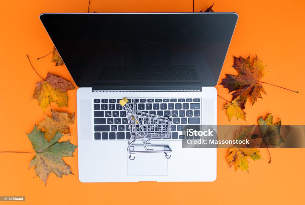 laptop computer and shopping cart laptop computer and shopping cart with autumn maple leaves aroung at orange background Above Stock Photo