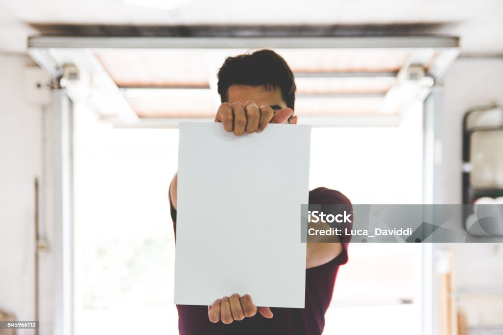 Young Adult Man Holding White Paper Young Adult Man Holding White Paper with geometric perspective in background Holding Stock Photo