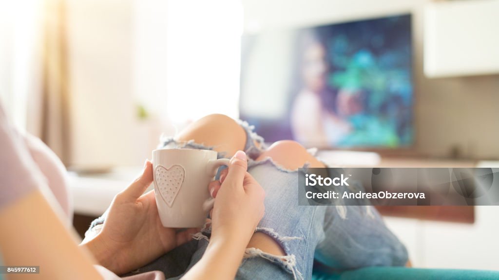 Jovem mulher relaxante no sofá em casa, assistindo tv - Foto de stock de Assistir TV royalty-free