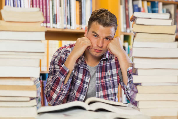 istock Irritated handsome student studying between piles of books 845988294