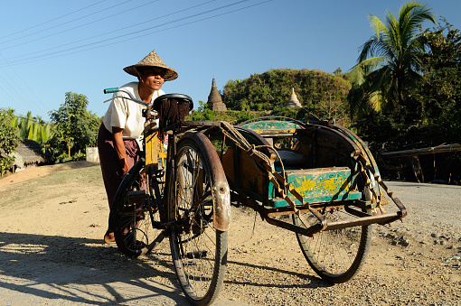 MRAUK-U, MYANMAR - 25 JANUARY 2011: The driver of the rickshaw is pumping the wheel up on a dirt road in Burma