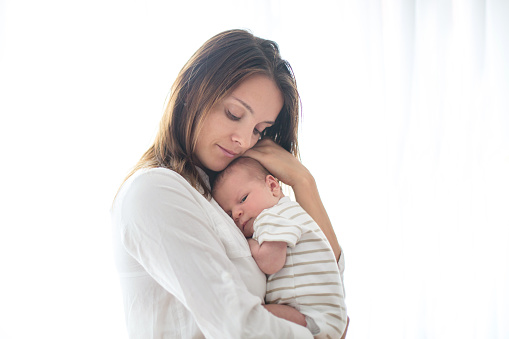 Young mother, holding her newborn baby boy at home in living room, back lit