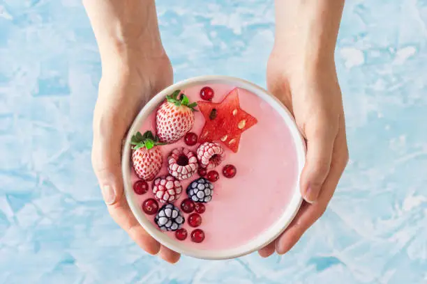 Photo of Woman's Hands Holding Pink Yogurt Smoothie Bowl with Berries and Watermelon