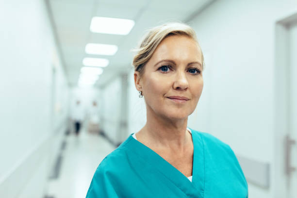 Female healthcare worker standing in hospital corridor Close up portrait of female healthcare worker standing in hospital corridor. Caucasian woman in hospital hallway staring at camera. female nurse photos stock pictures, royalty-free photos & images