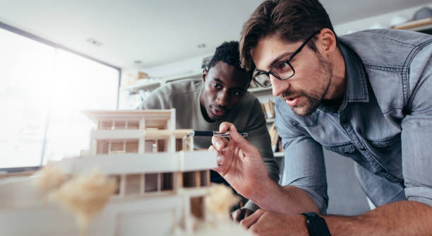 Two male architects discussing over house model Two male architects in office discussing over house model. Architect working on an architectural model. architect stock pictures, royalty-free photos & images