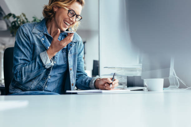 Smiling young businesswoman working at her desk Young female executive working in office. Smiling young businesswoman talking on cellphone and writing notes. Happy Customer stock pictures, royalty-free photos & images