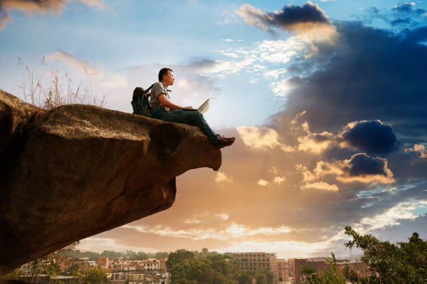 Man standing at the edge of a cliff using laptop