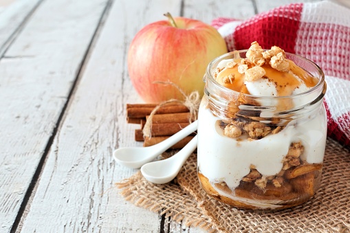 Sweet baked apple parfait in a mason jar on a rustic white wood background