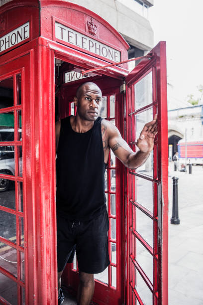Athlete stepping out of a bright red telephone booth after making a phone call to his friends, taking a break from a workout.