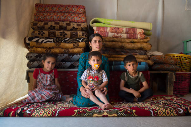 Yazidi mother and children in IDP camp Sharya, Iraq - May 28, 2017: A young Yazidi woman sits with her three children inside a tent in Sharya IDP camp in northern Iraq. They and their families fled the 2014 ISIS advance in which many Yazidis were killed and others, especially women and children, captured and trafficked by ISIS. islamic state stock pictures, royalty-free photos & images