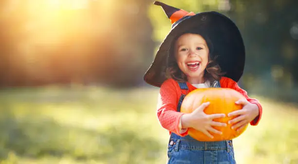 Photo of child girl with pumpkin outdoors in halloween