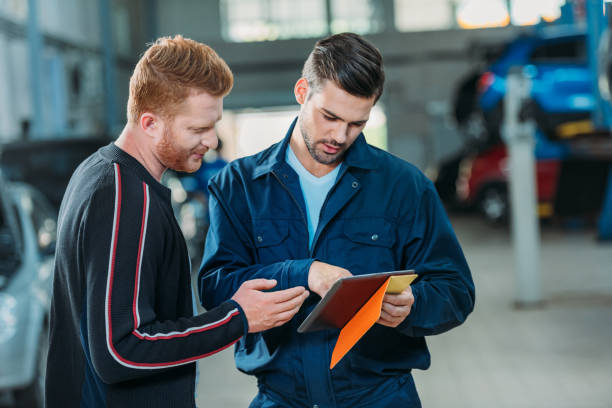 Automechanic and client looking digital tablet Young automechanic and client looking at the digital tablet at a repair shop. auto repair shop mechanic digital tablet customer stock pictures, royalty-free photos & images