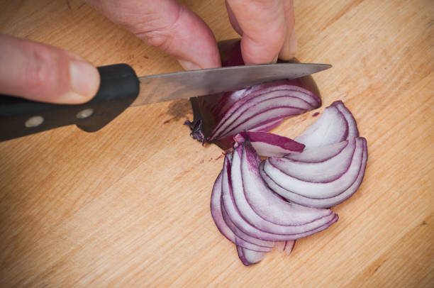 man cutting a purple onions on wooden cutting board